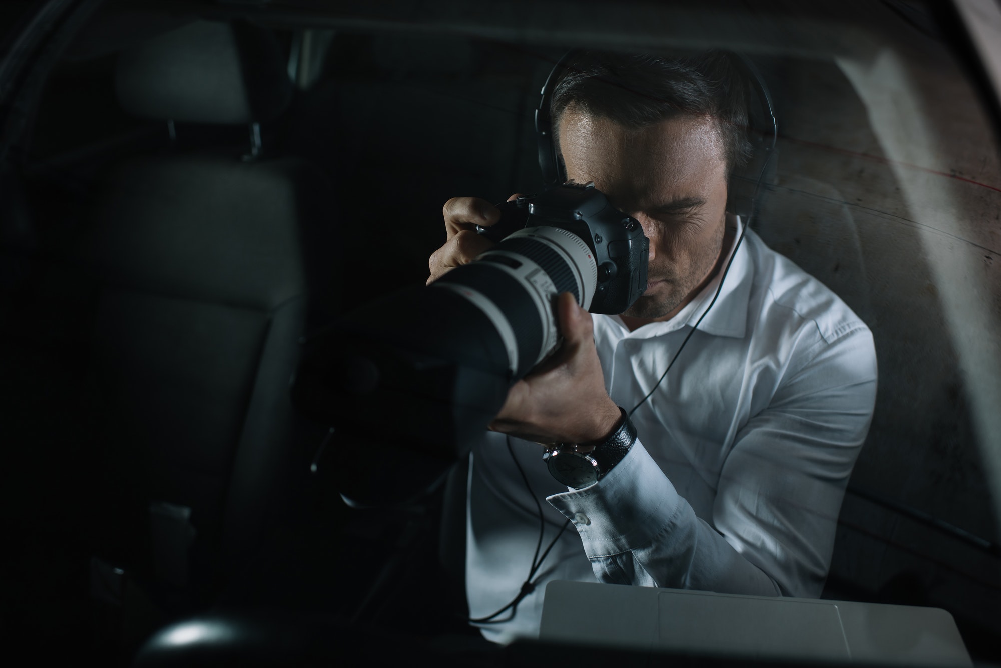 focused male private detective in headphones doing surveillance by camera from car